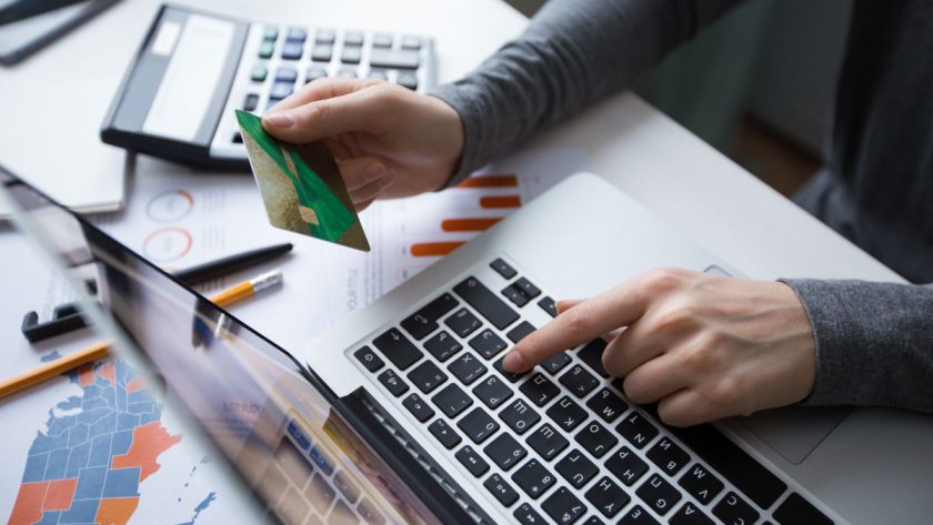 Widok z góry na osobę trzymającą zieloną kartę płatniczą i wpisującą dane na klawiaturze laptopa.