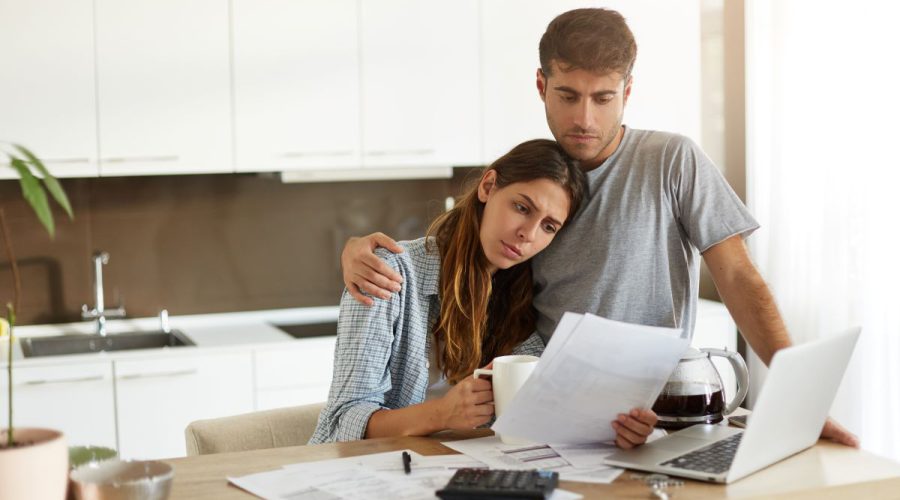 Zasmucona para siedzi przy kuchennym stole, analizując dokumenty finansowe przed otwartym laptopem - odmowa przyznania kredytu.