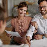Uśmiechnięta młoda para podaje rękę doradcy finansowemu po udanym podpisaniu umowy na zielony kredyt.