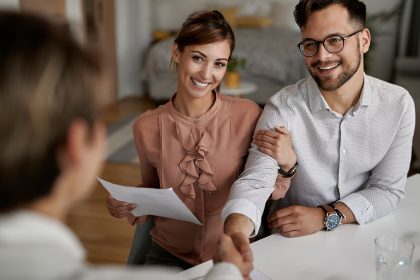 Uśmiechnięta młoda para podaje rękę doradcy finansowemu po udanym podpisaniu umowy na zielony kredyt.