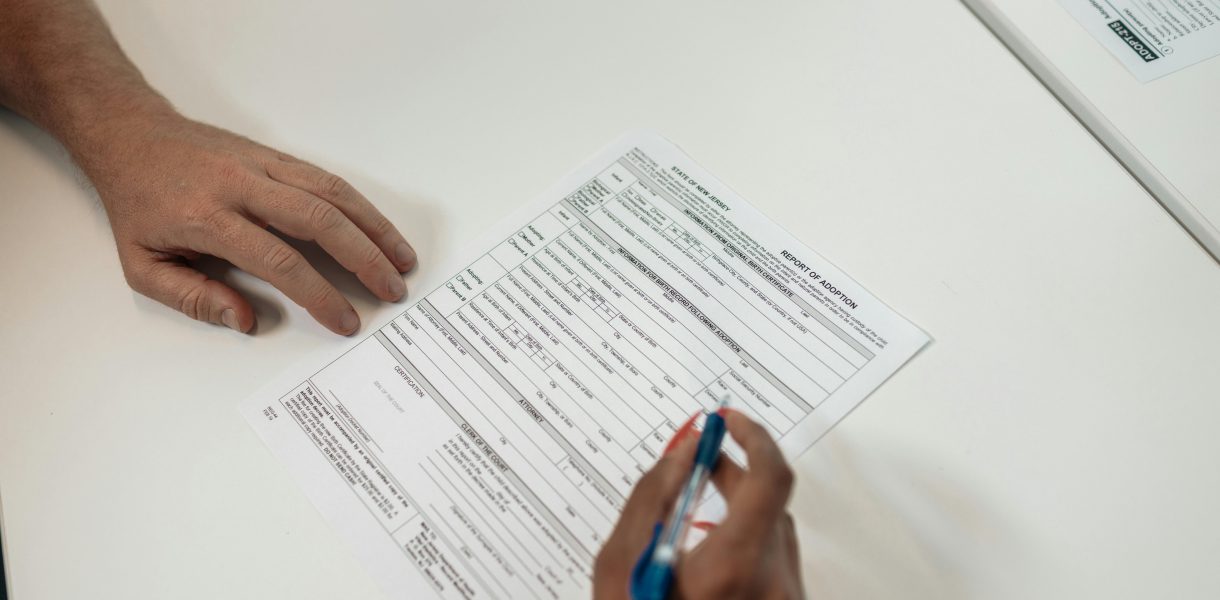 Osoba analizująca oficjalną umowę kredytową na białym biurku, zbliżenie na dłonie i dokumenty.