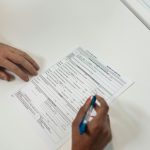 Osoba analizująca oficjalną umowę kredytową na białym biurku, zbliżenie na dłonie i dokumenty.