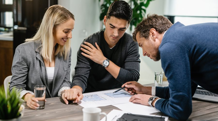 Doradca finansowy wskazuje na dokumenty i omawia plan inwestycyjny z dwojgiem młodych przedsiębiorców przy drewnianym stole.