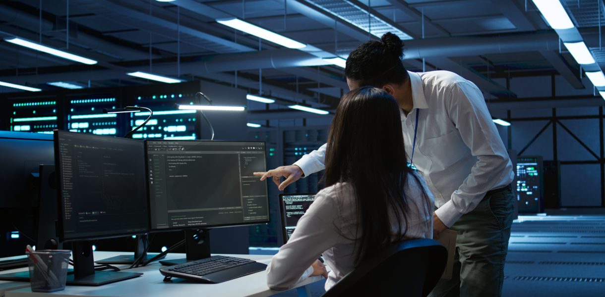 Dwoje specjalistów ds. cyberbezpieczeństwa analizuje kody i logi systemowe na monitorach w centrum operacyjnym banku.