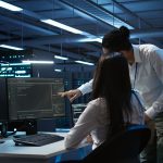Dwoje specjalistów ds. cyberbezpieczeństwa analizuje kody i logi systemowe na monitorach w centrum operacyjnym banku.
