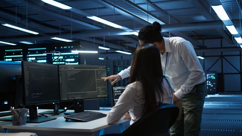 Dwoje specjalistów ds. cyberbezpieczeństwa analizuje kody i logi systemowe na monitorach w centrum operacyjnym banku.