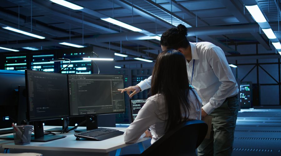 Dwoje specjalistów ds. cyberbezpieczeństwa analizuje kody i logi systemowe na monitorach w centrum operacyjnym banku.